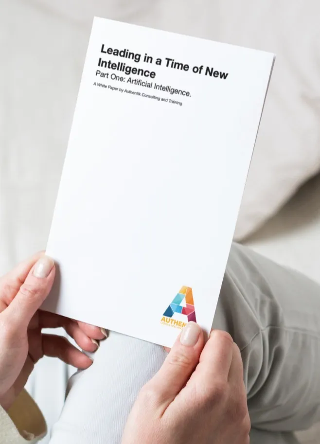 A person holding Authentik's White Paper in their lap. The title is "Leading in a Time of New Intelligence"