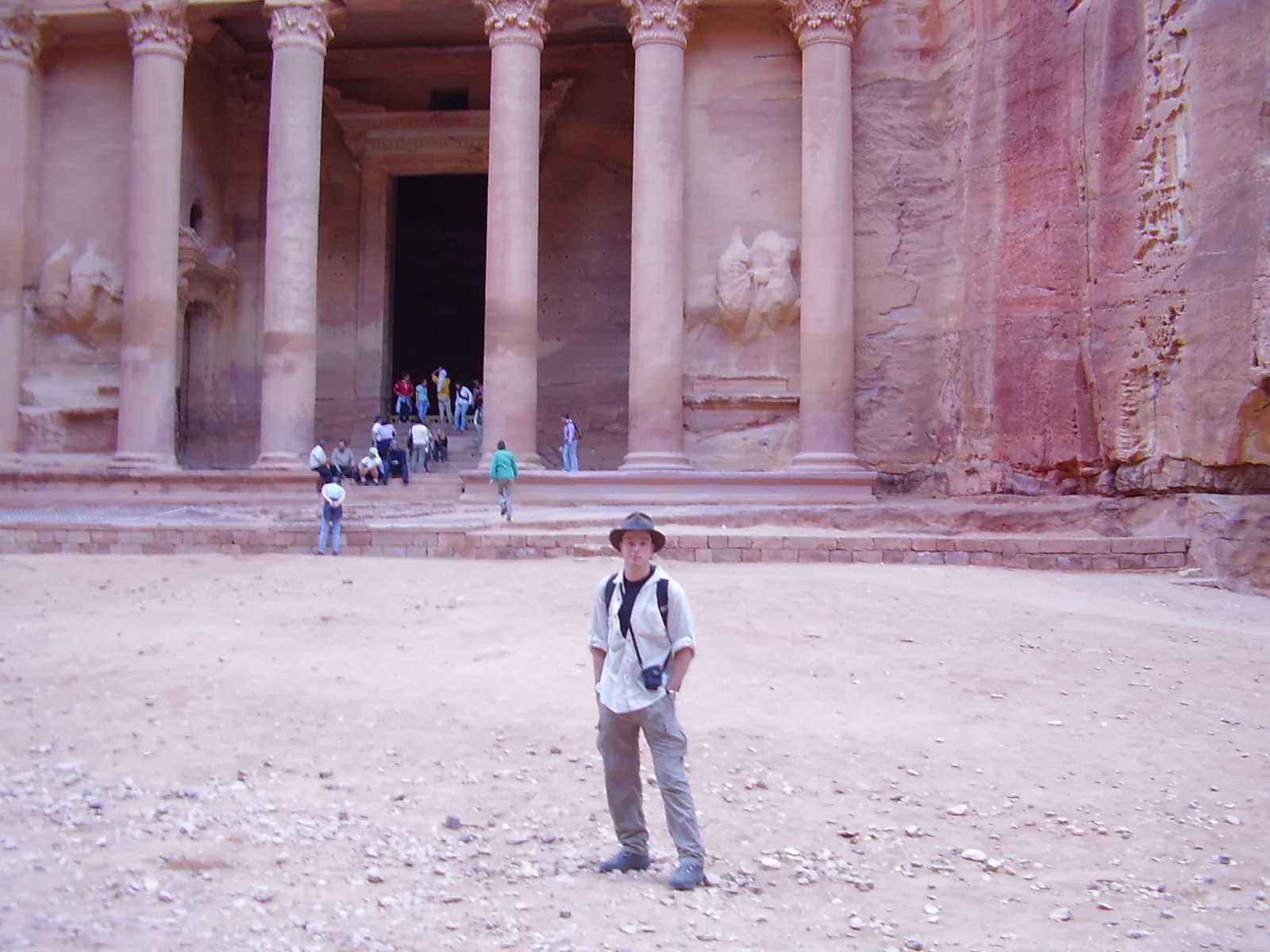 A traveller standing in the open sand in front of the carved rock facade of the Treasury at Petra.