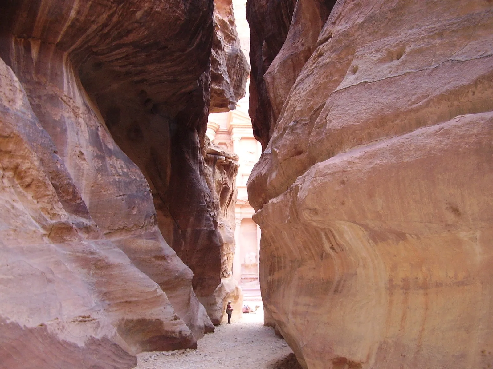 The narrow Siq canyon at Petra, with the Treasury just visible through the gap at the far end.