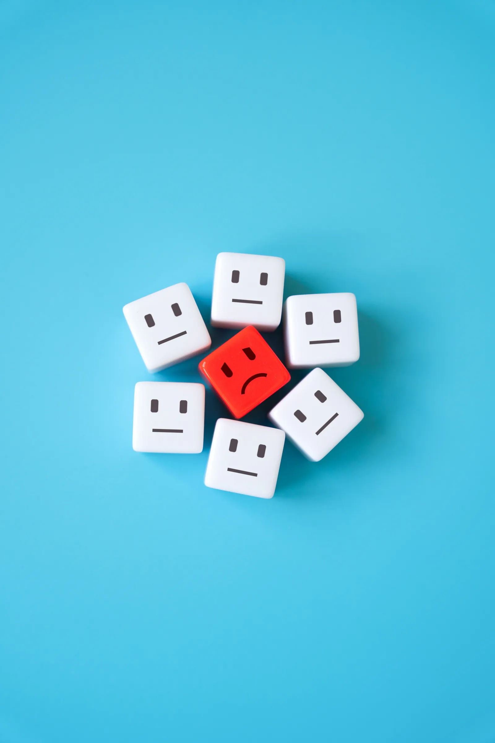 Seven white blocks with neutral faces arranged in a ring around a single red block with a frowning face.