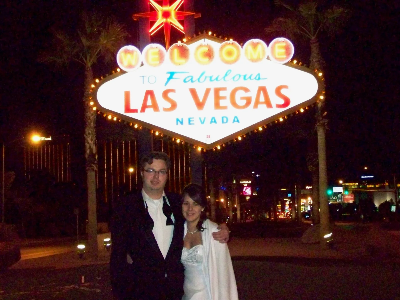 A couple standing in front of the iconic Las Vegas sign at night.