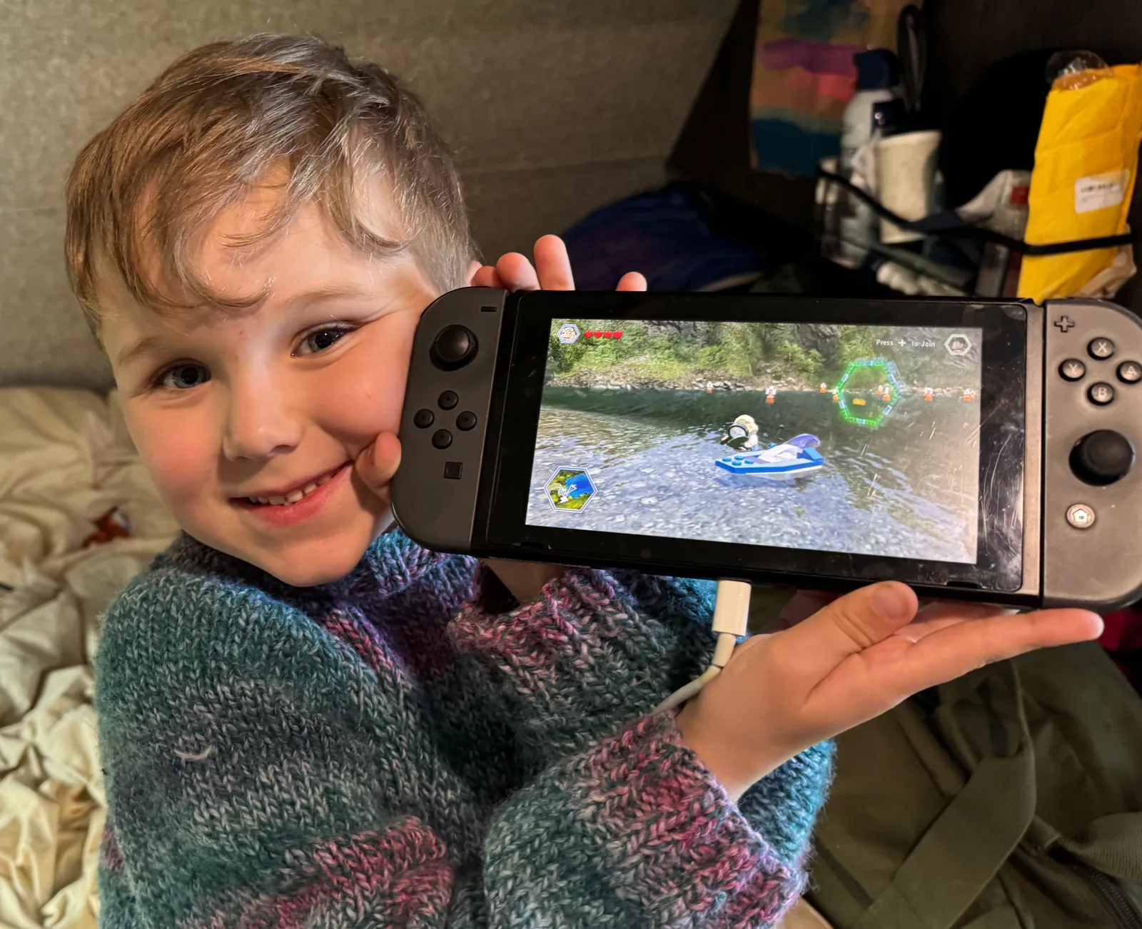 A child showing his Nintendo Switch to the camera with a big smile on his face