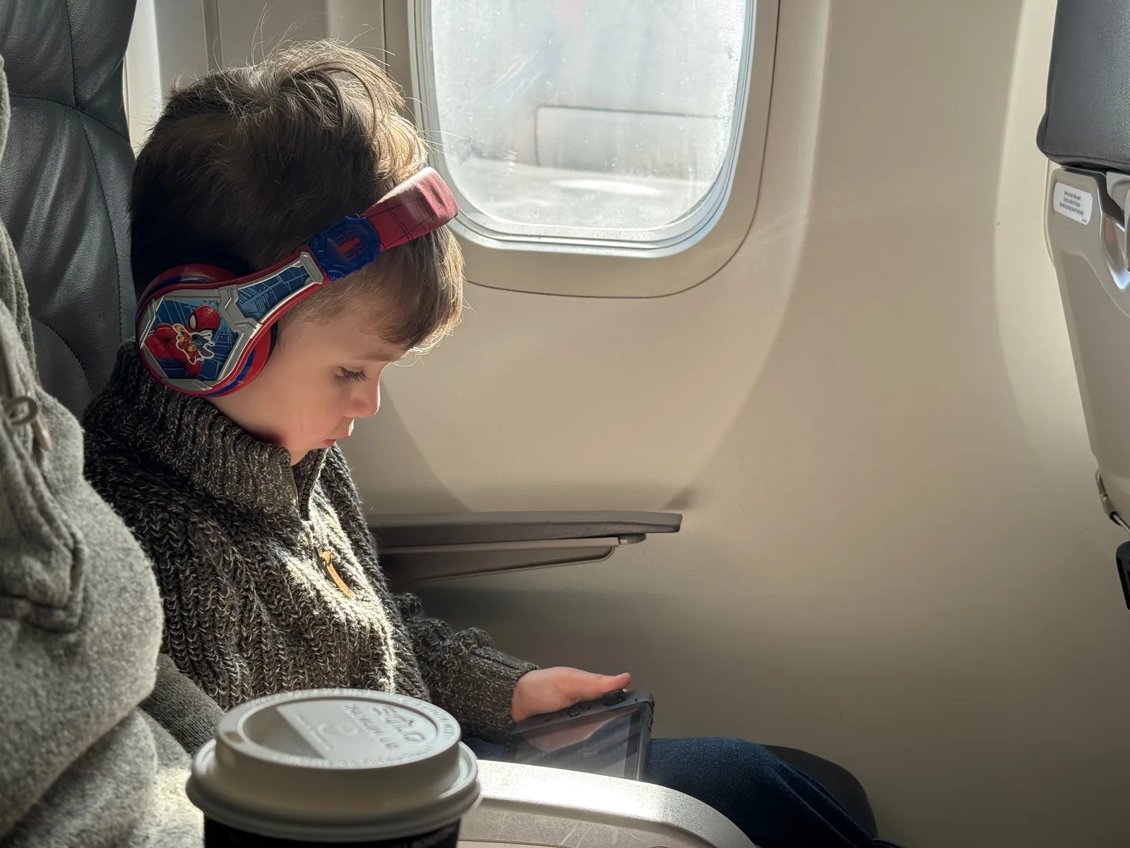 A child on an airplane playing a nintendo with spiderman headphones