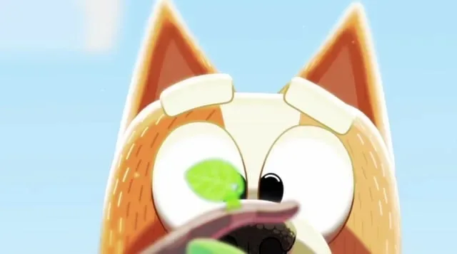 A close-up of Bingo from Bluey holding a small green leaf up to her face.
