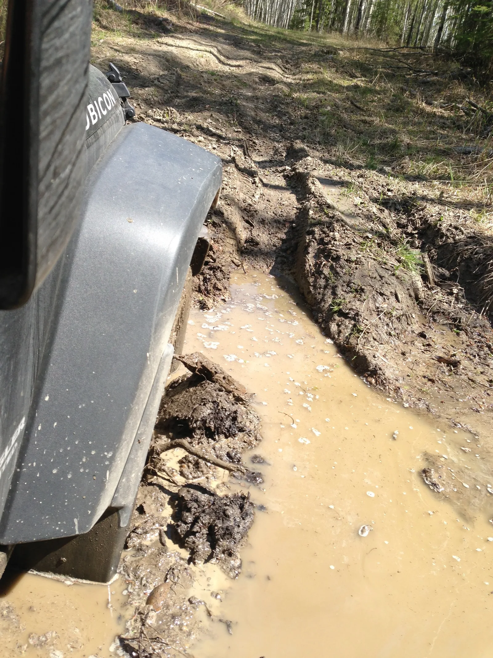 An image of a jeep bogged down in mud, taken from the passenger seat showing the mudpit and the front left wheel.