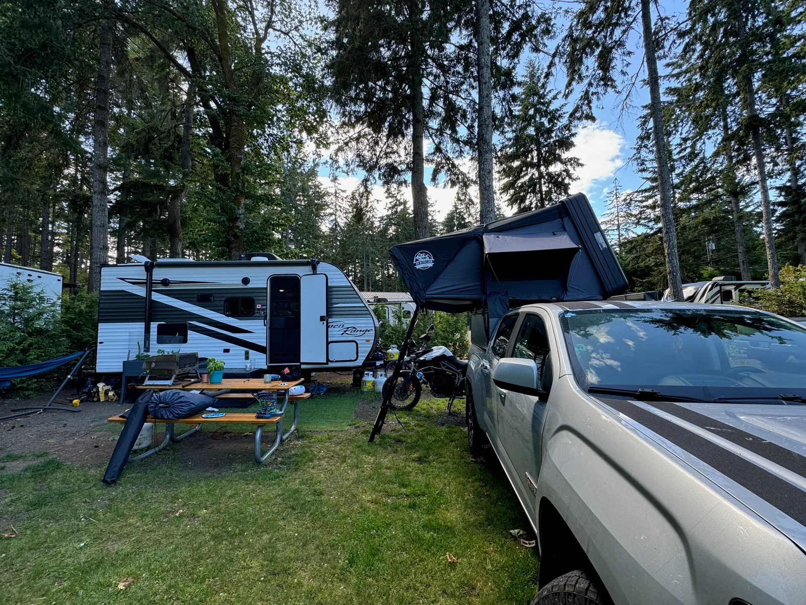 An RV, a motorbike, and a pickup truck with a roof tent.
