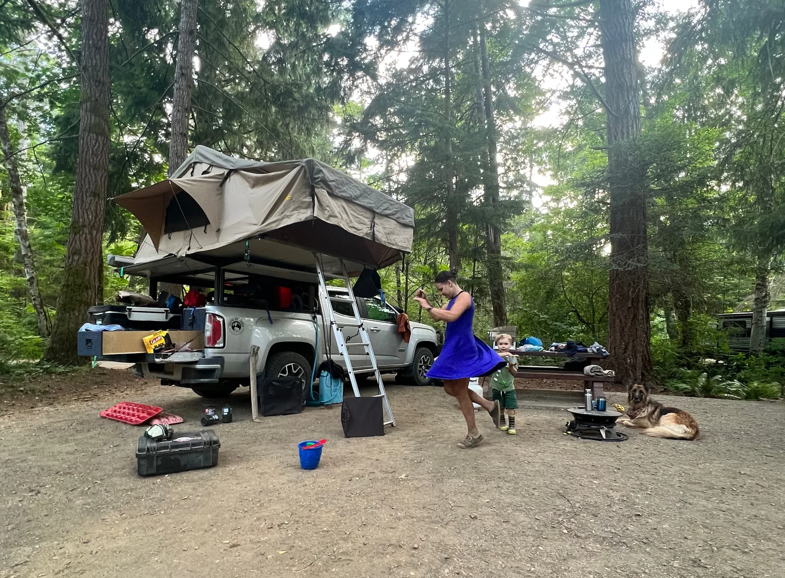 A woman and child dancing next to a truck with a rooftent.