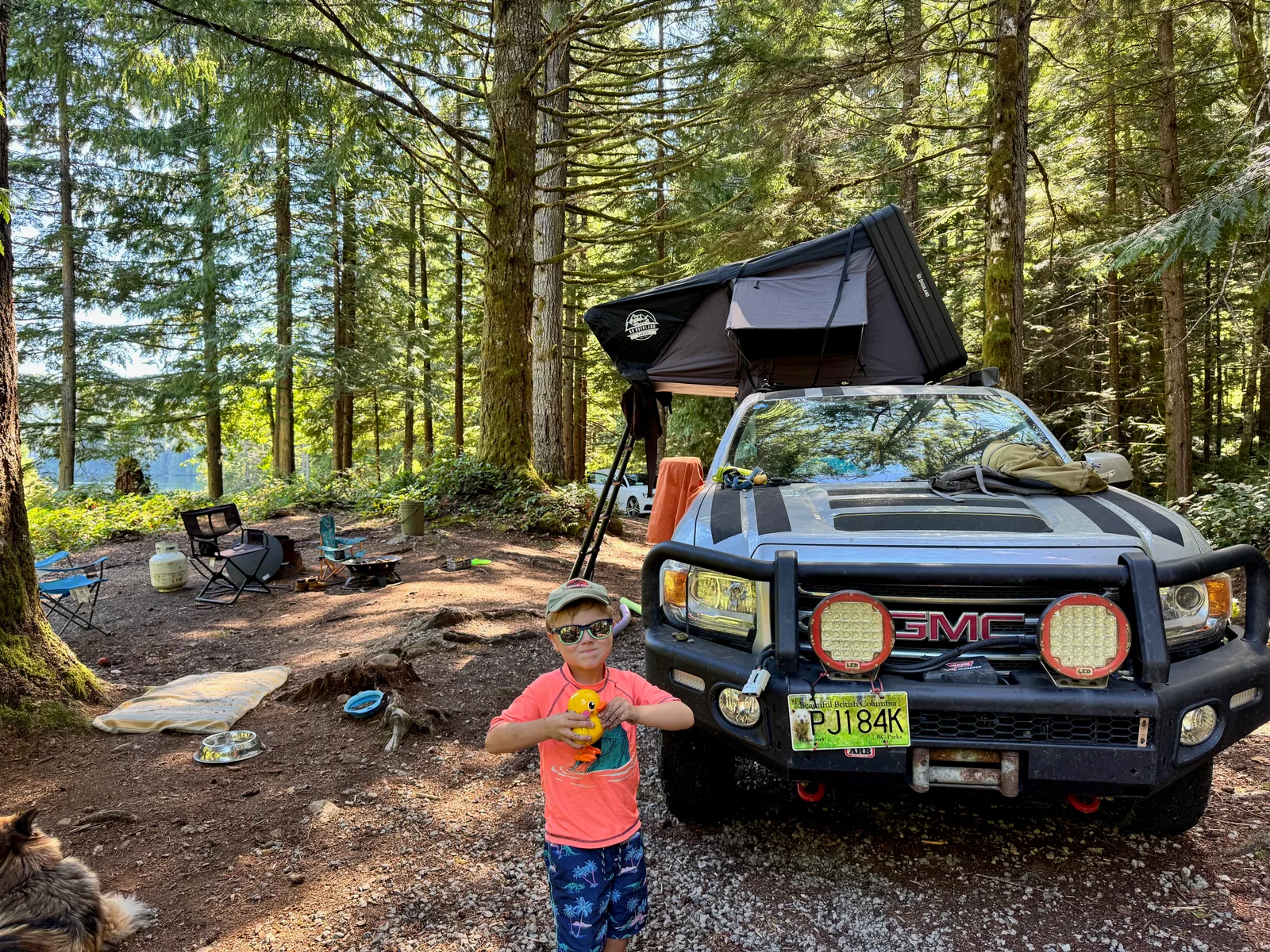 A young boy next to a truck with a roof tent.