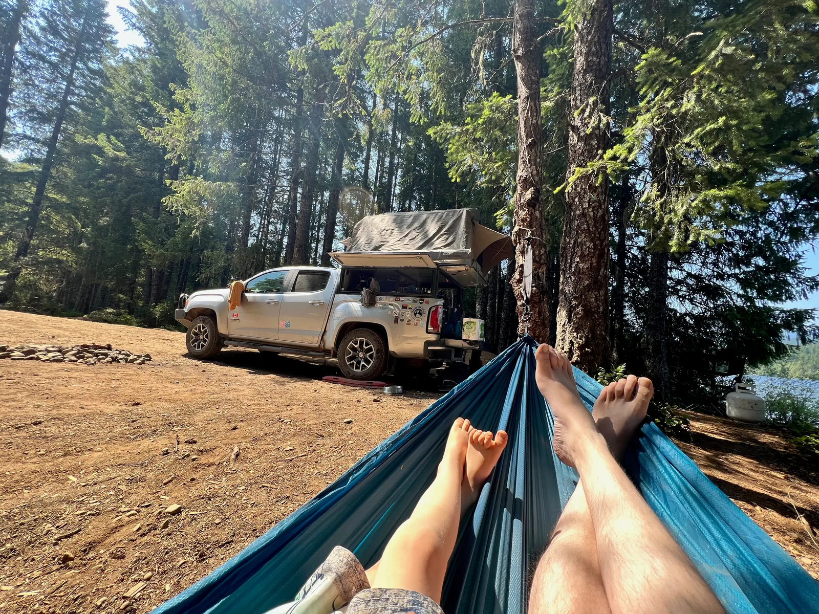 a father and son in a hammock with only their legs showing, looking at an Overland-ready 4x4 truck at a campsite.