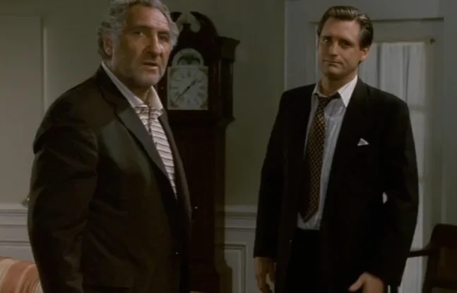 A film still of two men in suits standing in a panelled room beside a grandfather clock.