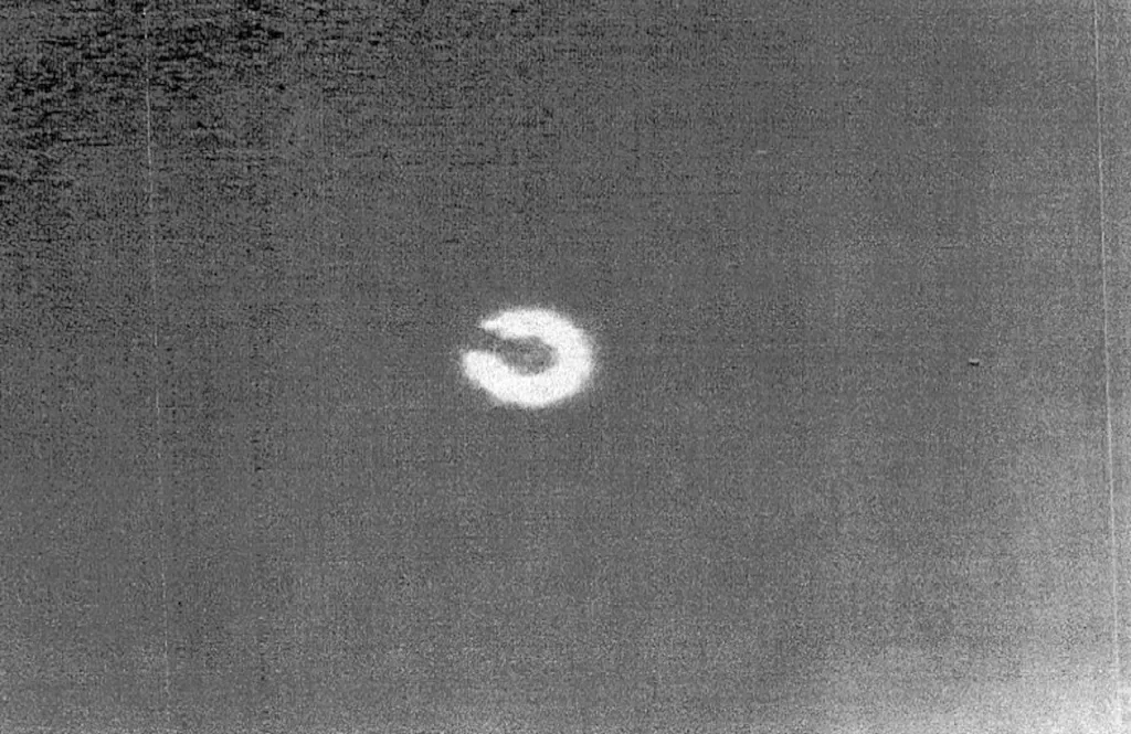 A horseshoe-shaped object on a thermal camera, white on a grey background.