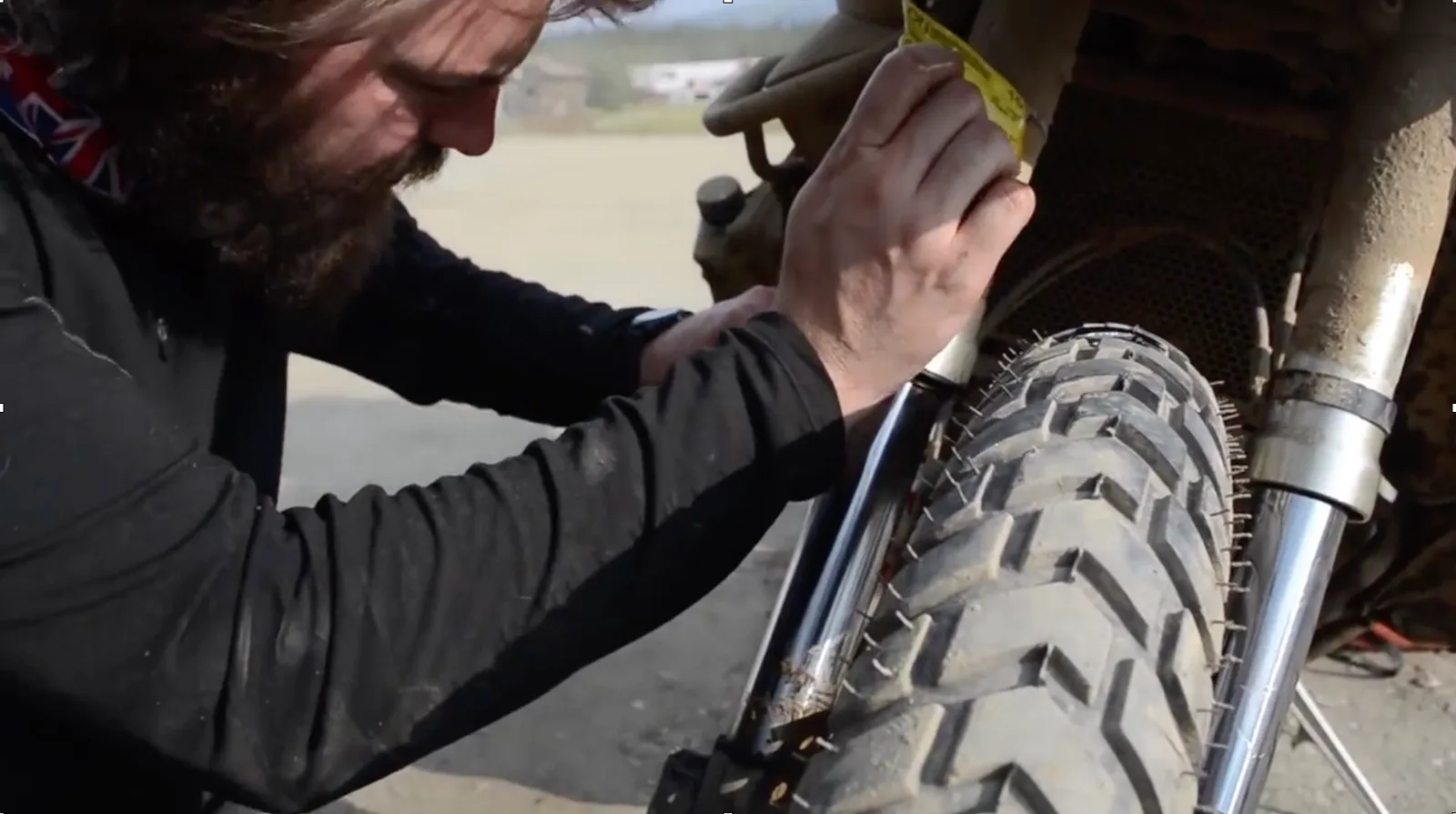 A motorcyclist using some makeshift tools to repair the front suspension of his bike.
