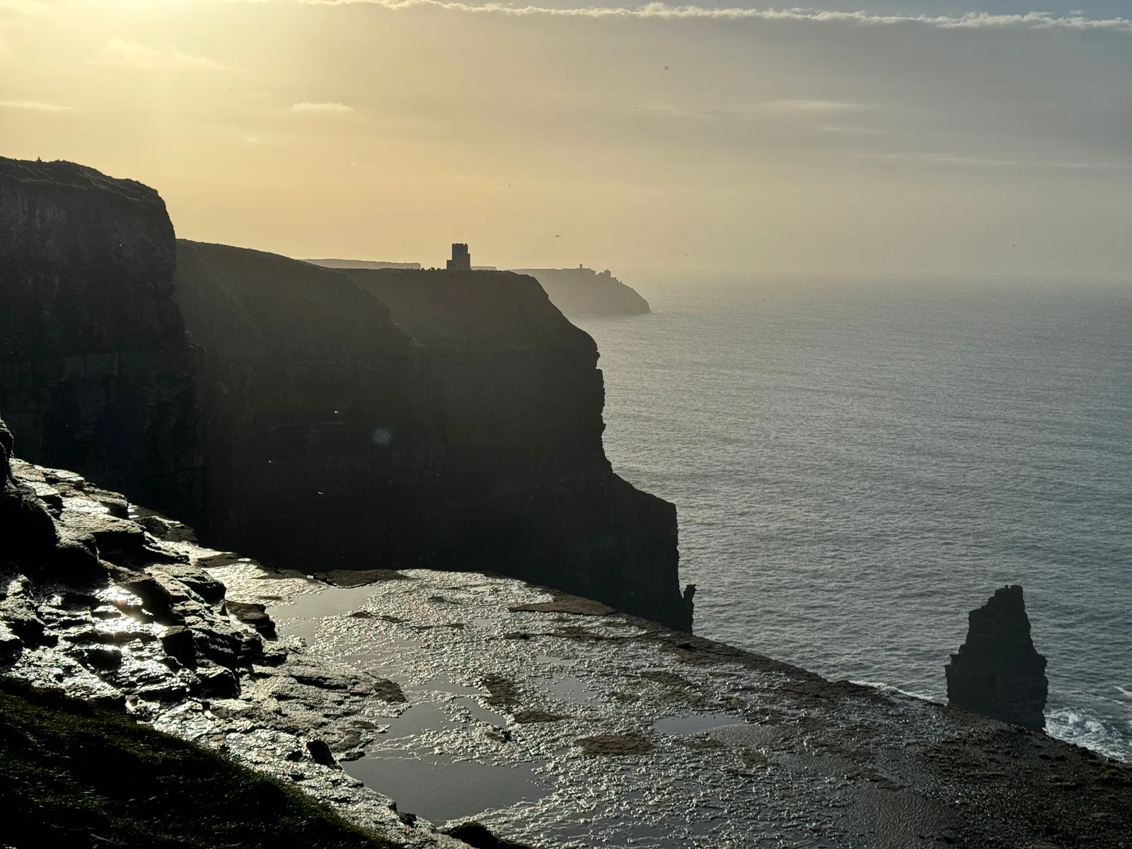 The Cliffs of Moher at sunset, with O'Brien's Tower on the headland and a sea stack rising out of the water.